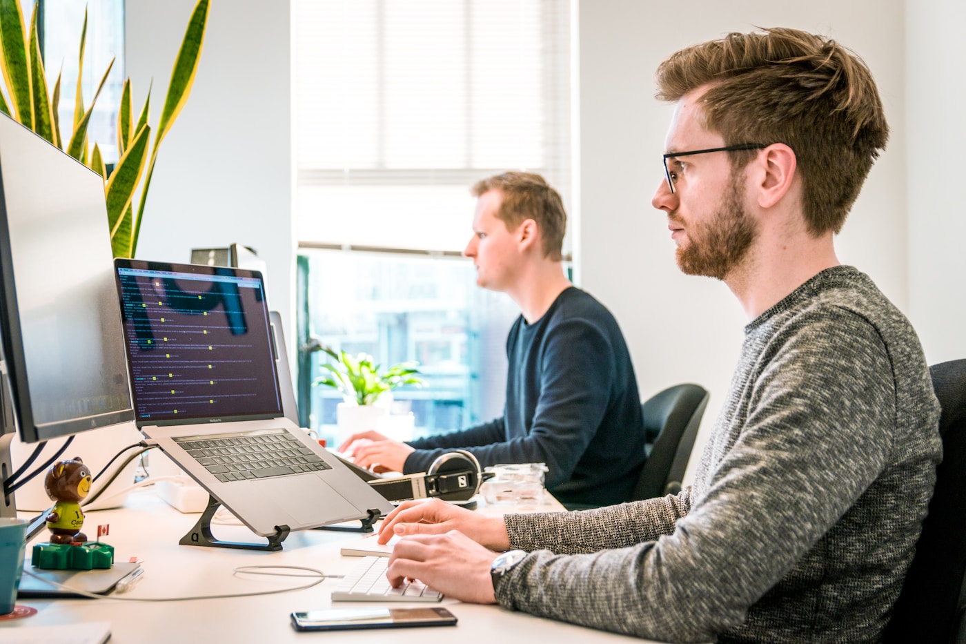 Two analysts working side by side at code and dashboard screens in a bright office